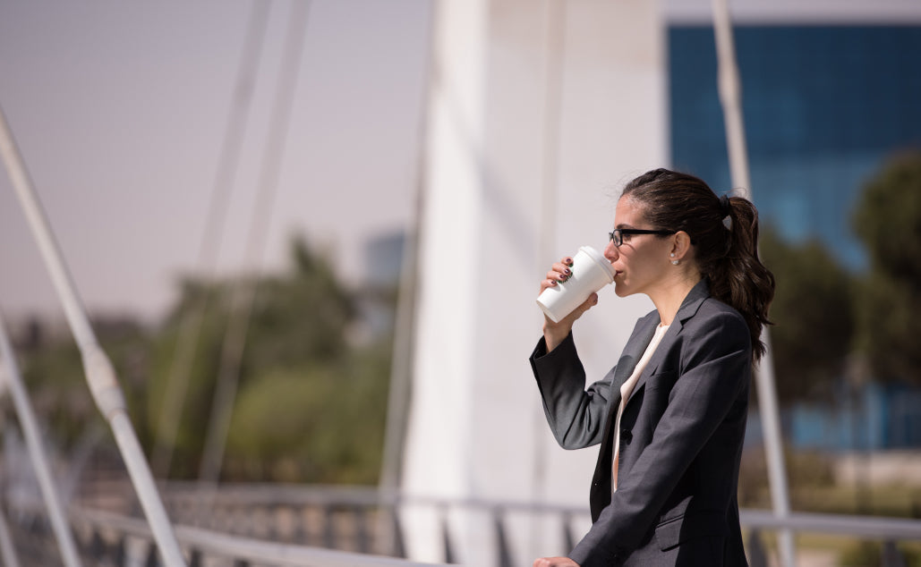Professional woman in a grey blazer drinking coffee while reflecting outdoors.