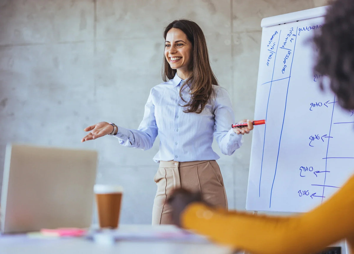 Smiling female executive coach presenting a strategy on a whiteboard during a workshop.